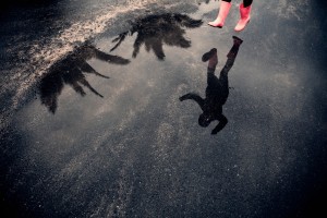 Reflection of person in rubber boots jumping over puddle
